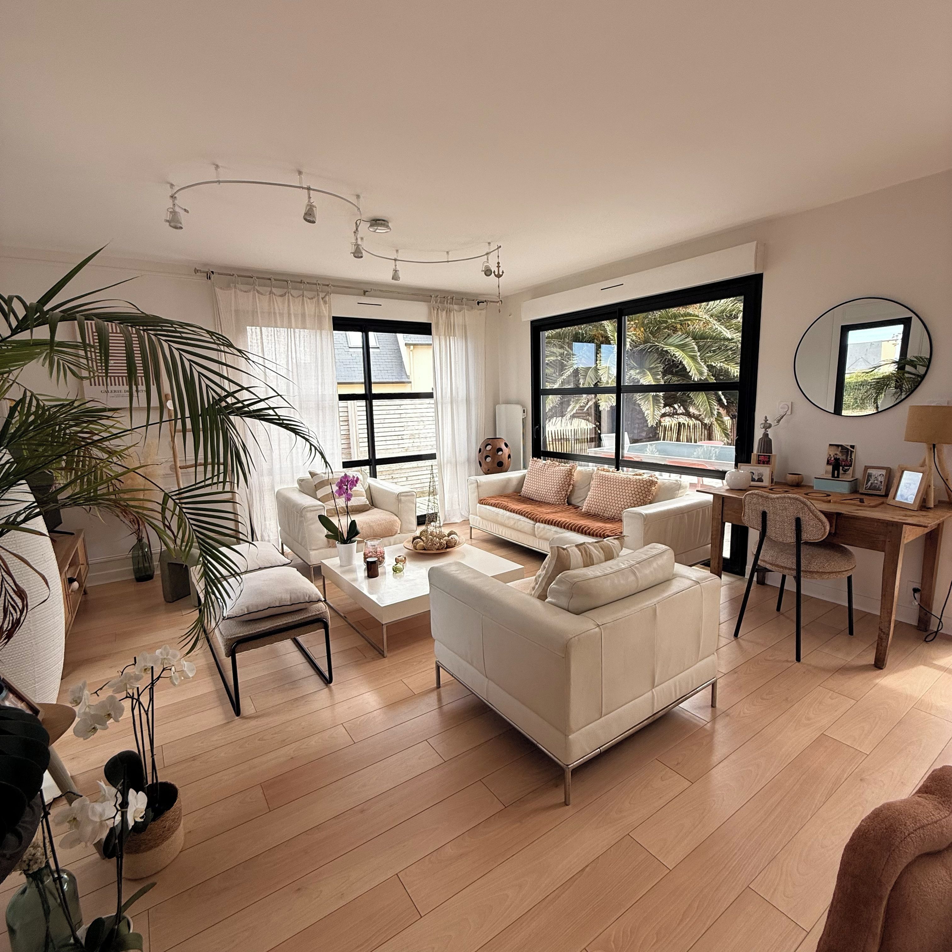 Ein geräumiges Wohnzimmer mit großem Fenster, einem weißen Sofa, einem Couchtisch und einem Holztisch.