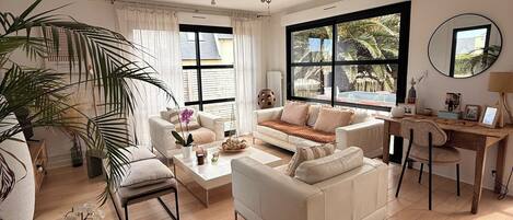 Ein geräumiges Wohnzimmer mit großem Fenster, einem weißen Sofa, einem Couchtisch und einem Holztisch.