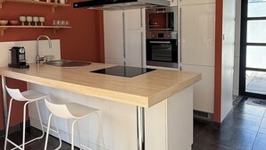 A modern kitchen with a central island, stainless steel appliances, and a red accent wall. - Single-storey house, close to the port and Kerdéniel beach. (Ploudalmézeau)