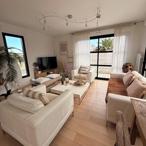 A modern living room with a flat-screen TV, sofas, a coffee table, and a large window with a view of the outdoors.