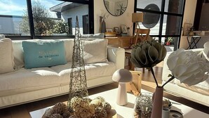 A modern living room with a white sofa, a coffee table with decorative items, and large windows offering a view of the outdoors. - Single-storey house, close to the port and Kerdéniel beach. (Ploudalmézeau)