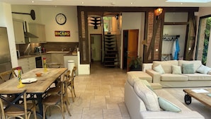 A modern kitchen with a dining area, a sofa, and a staircase leading to a loft.