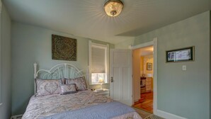 A bedroom with a bed, a nightstand, a door, and a hallway leading to another room.