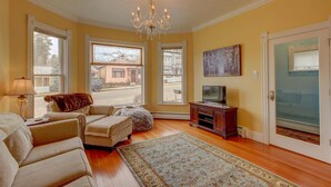 A living room with a chandelier, large windows, a television, and a rug.