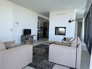 A modern living room with a sofa set, a television, and a kitchen in the background.
