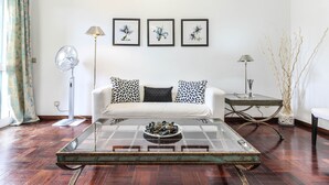Ein Wohnzimmer mit einem weißen Sofa, einem Glastisch und drei gerahmten floralen Kunstwerken an der Wand.