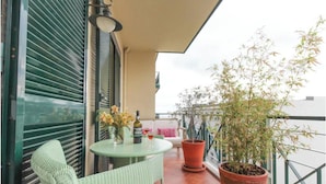Ein Balkon mit Tisch, Stühlen, einer Topfpflanze und einer Weinflasche.