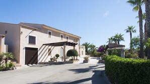 A Mediterranean-style villa with a covered patio, palm trees, and a stone pathway. - Typical Majorcan finca with pool, wireless, garden, barbecue and heating (Santanyi)
