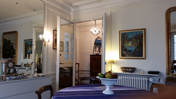 A dining area with a table set for two, a chandelier, a painting on the wall, and a mirror reflecting part of the room.