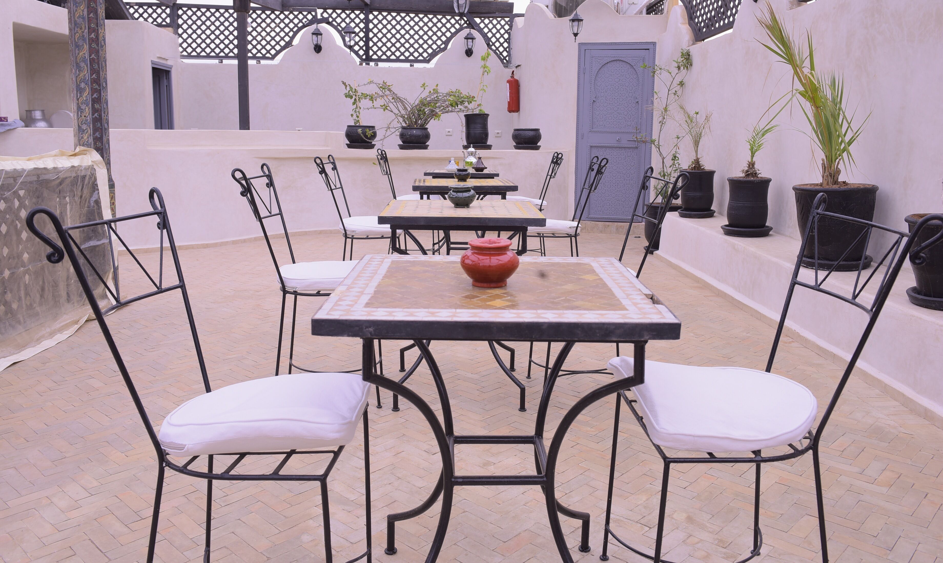 An outdoor patio with tables and chairs, potted plants, and a blue door.