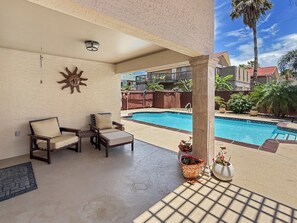 A covered outdoor area with a pool, lounge chairs, and potted plants.