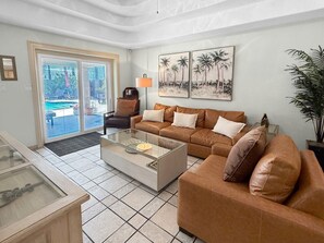 A living room with a glass coffee table, two sofas, a chair, and a large window with a view of a pool.