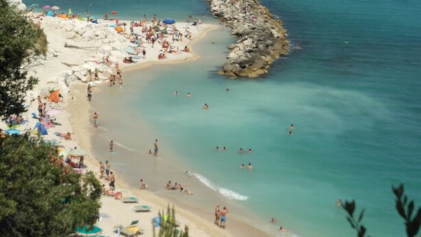 Ein Strand mit klarem türkisblauem Wasser, Felsen und Menschen, die die Sonne genießen.