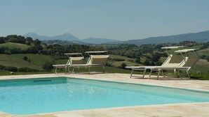 Ein Pool mit Liegestühlen und Blick auf sanfte Hügel und Berge.