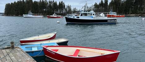 A dock with several small boats moored, a larger boat with the number 94913 in the background, and a forested shoreline.