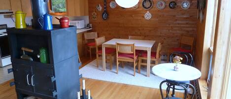 A cozy cabin interior with a wood stove, dining table, chairs, and a variety of decorative plates on the wall.
