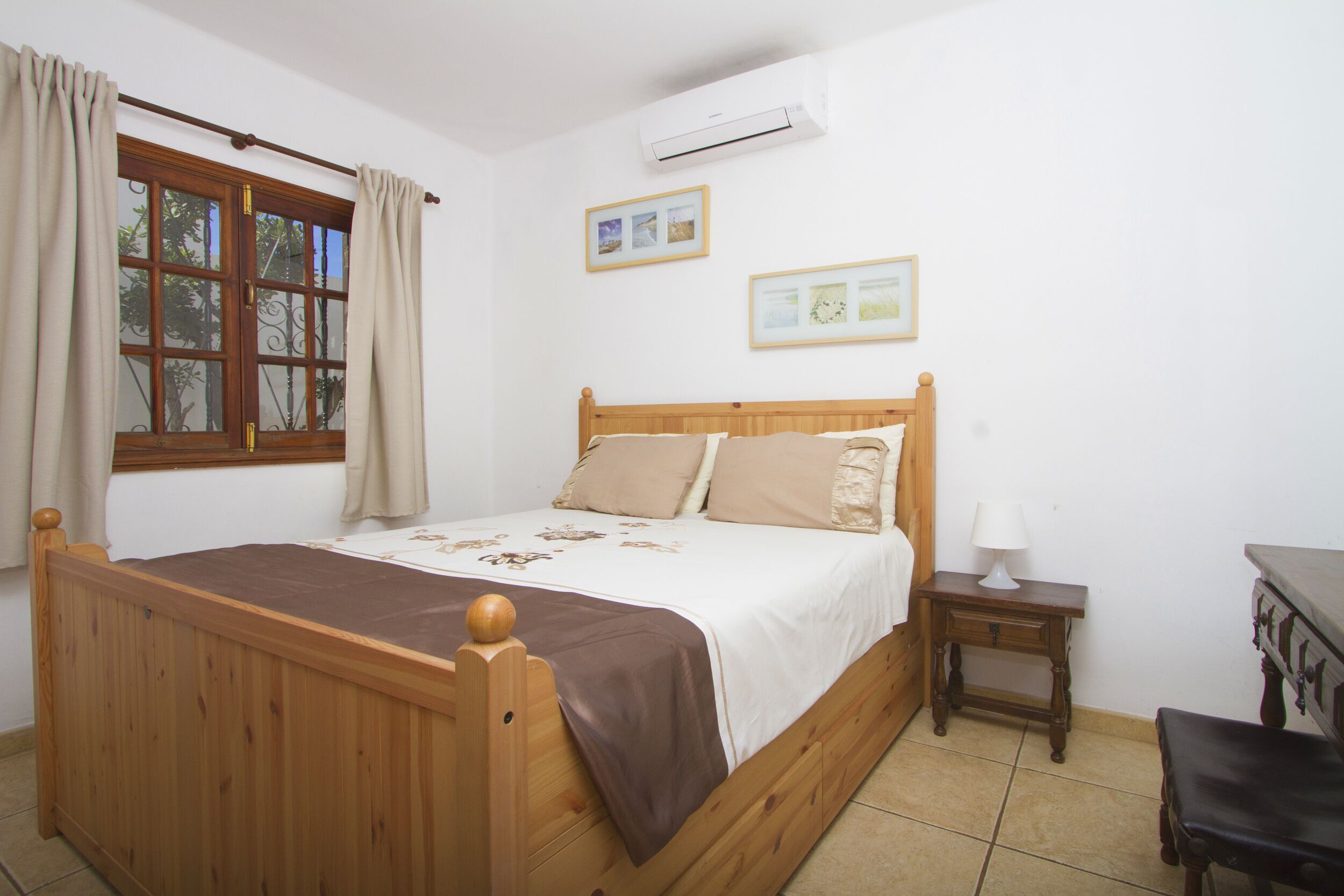 A wooden bed with a headboard, a bedside table with a lamp, and a window with curtains.