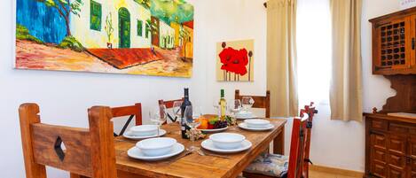 A dining area with a wooden table set for four, surrounded by chairs. A colorful painting and a red abstract artwork are on the wall.