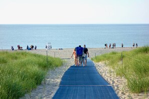 A sandy beach with a blue mat leading to the water, surrounded by grass and a rope barrier.
