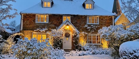 Una casa de dos pisos con un tejado cubierto de nieve y la silueta de una iglesia al fondo.