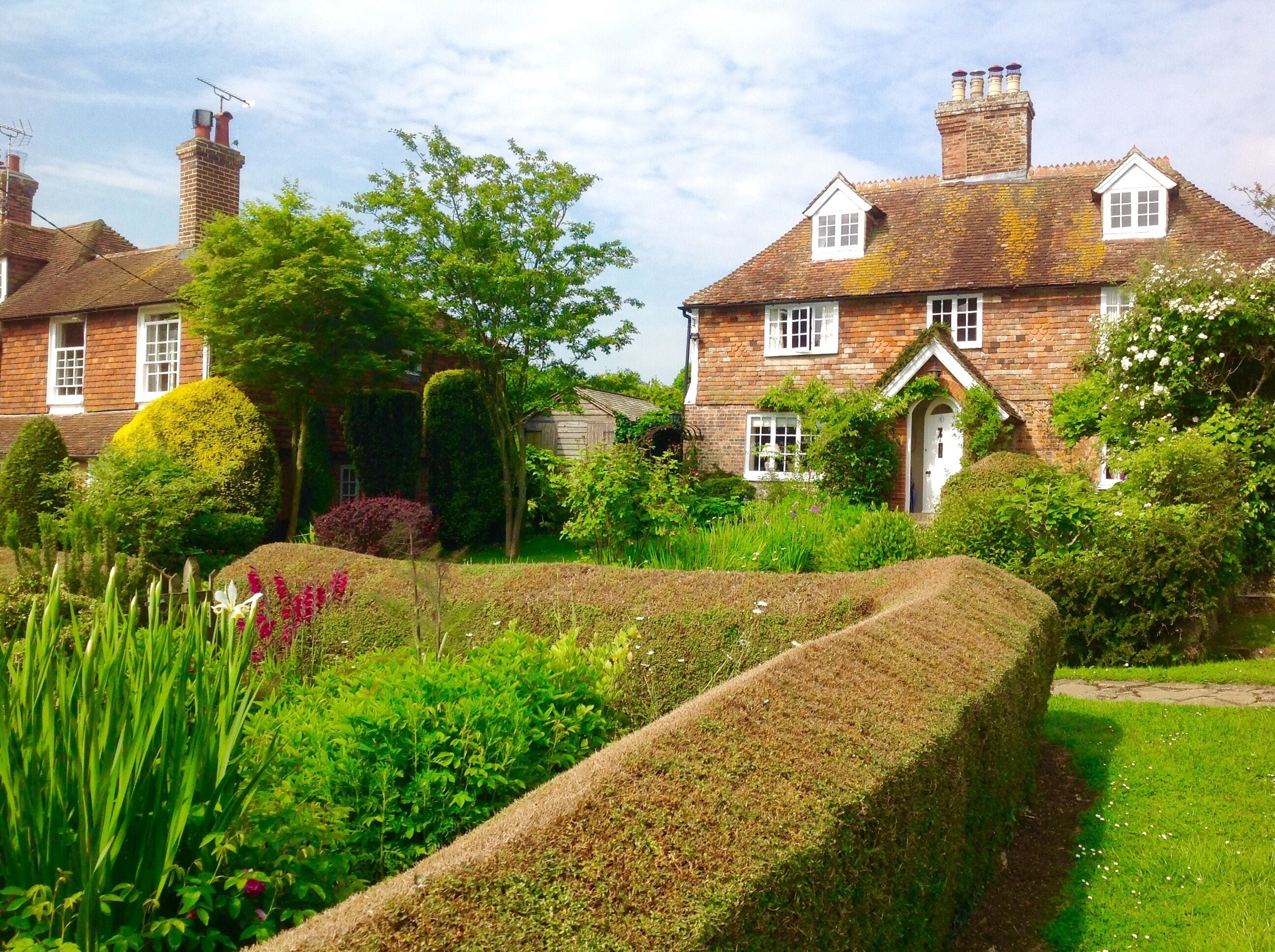 Une maison traditionnelle en briques, dotée d’un jardin bien entretenu, comprenant une haie et diverses plantes.
