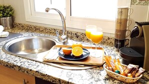A kitchen with a stainless steel sink, a coffee maker, a tray with orange juice, and a basket of snacks. - iloftmalaga Puerta del Mar IV (Málaga)