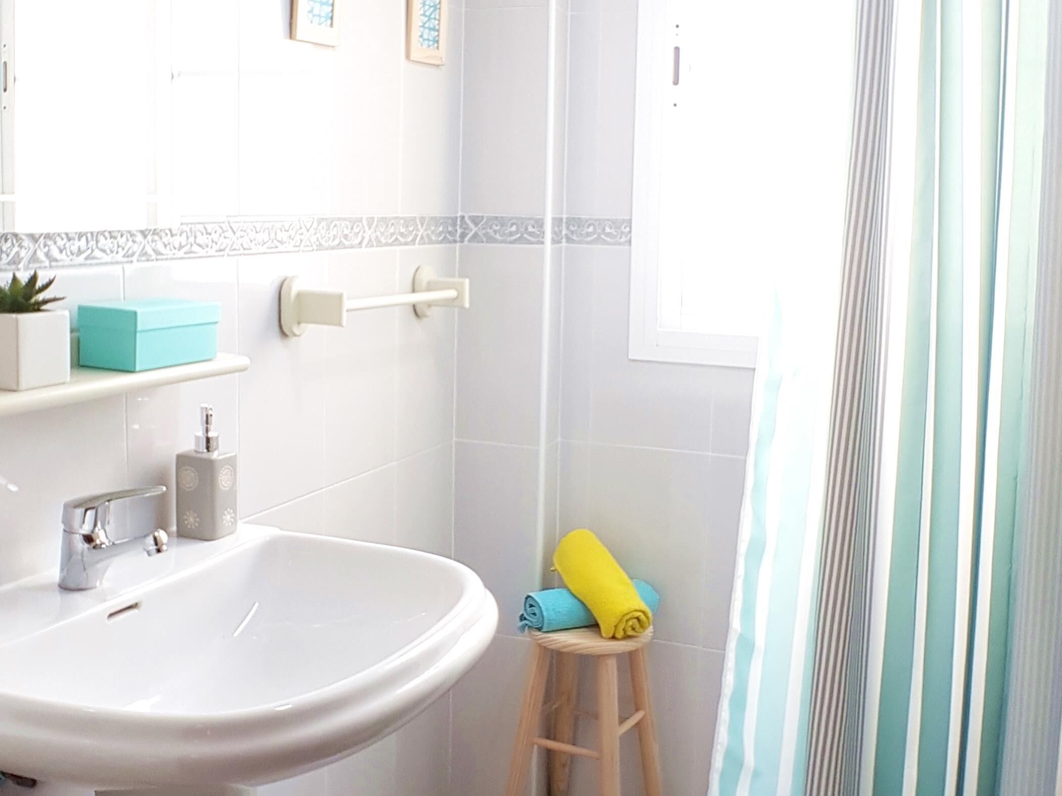 A bathroom with a white sink, a small stool, and a shower curtain.