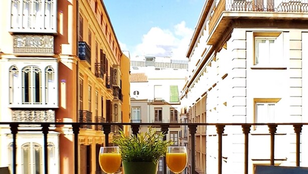 A balcony with a table, two glasses of orange juice, and a potted plant. - iloftmalaga Puerta del Mar IV (Málaga)