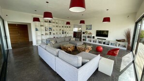 A modern living room with a sectional sofa, a glass coffee table, and red pendant lights. - VILLA LA LAGUNA-450 m²-Heated swimming pool-Natural park view-Wifi-12 px (La Oliva)