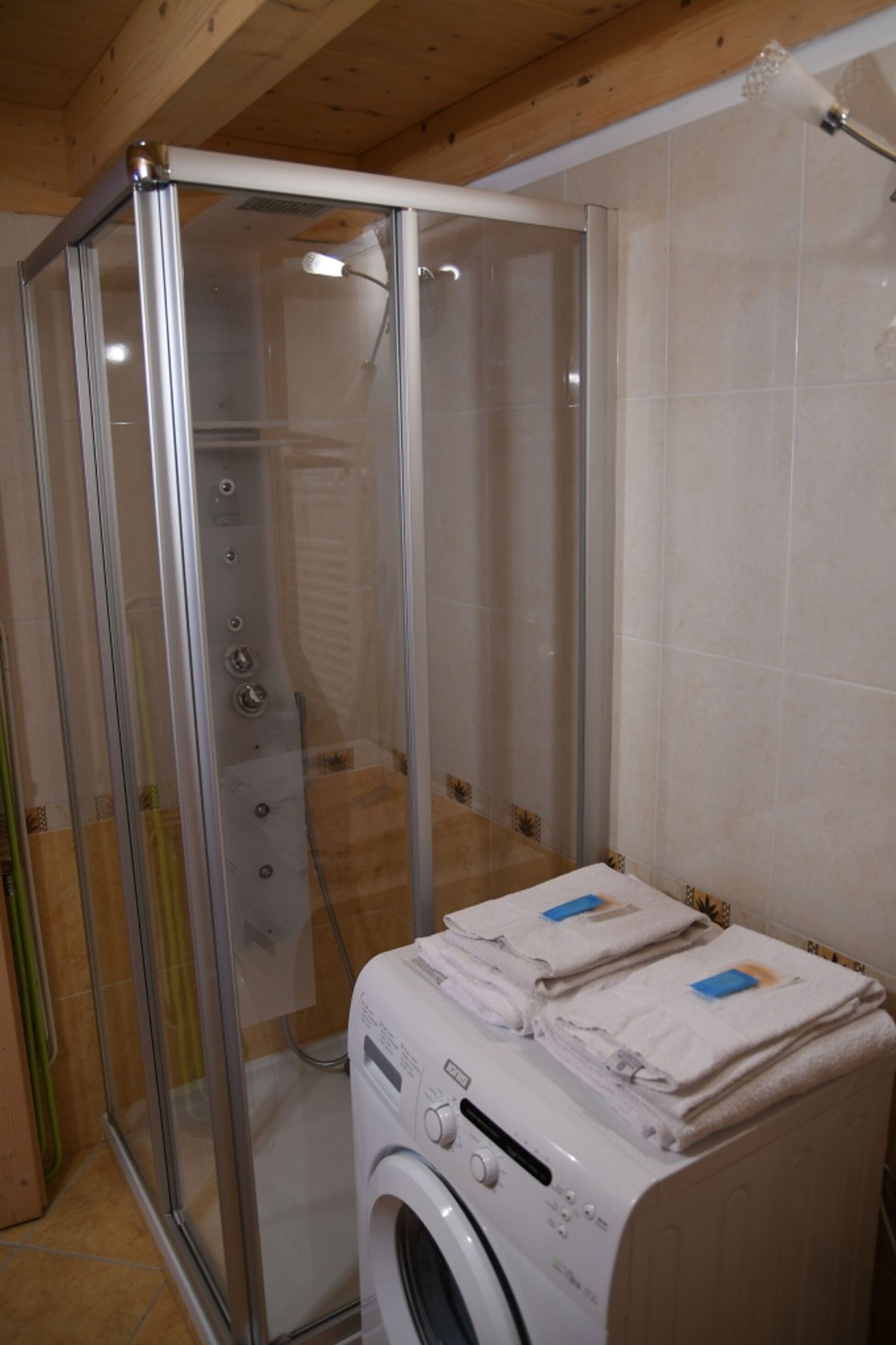 A compact bathroom with a glass shower enclosure, a washing machine, and a tiled wall.
