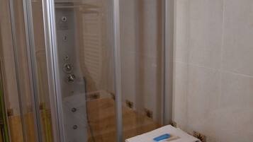 A compact bathroom with a glass shower enclosure, a washing machine, and a tiled wall.