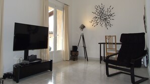 Un saló amb televisió, trípode, cadira i una peça decorativa a la paret.