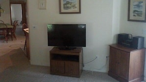A living room with a flat-screen TV on a wooden stand, a dining area with a table and chairs, and a framed picture on the wall. - Pet Friendly Home, Short Walk to the Beach! (1807) (Wellfleet)