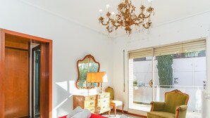 A hotel room with a bed, a chandelier, a mirror, a dresser, a chair, and a window with a view of greenery. - Bed&BCN Hills House with swimming pool (Barcelona)