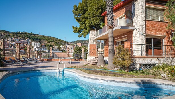 A swimming pool with a curved edge, surrounded by a stone and brick building with a balcony. - Bed&BCN Hills House with swimming pool (Barcelona)