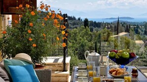 Ein Frühstückstisch mit Obstschale und Blick auf eine Landschaft mit Bäumen und einem Gewässer.
