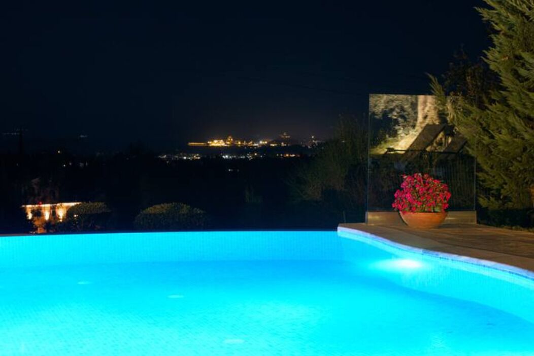 Una piscina por la noche con luces de ciudad al fondo.
