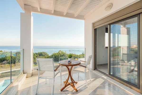 Uma varanda com mesa e cadeiras, porta de vidro e vista para o mar.