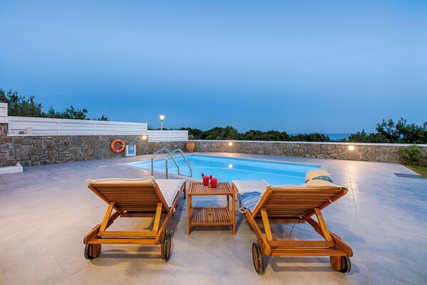 A poolside area with lounge chairs, a table with drinks, and a stone wall.