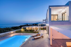A modern poolside area with a clear view of the sea, a pool, and lounge chairs.