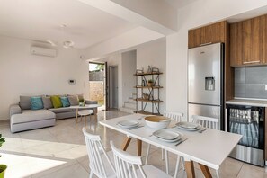 Cozinha moderna com frigorífico embutido, mesa de jantar com cadeiras, sofá e uma pequena escadaria que dá para uma área externa.
