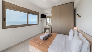 A hotel room with a bed, a TV, a wardrobe, and a window with a view of the sea. - Sea La vie Villa in Kiotari (RHODES)