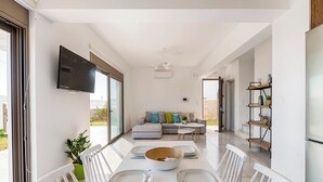 A modern living room with a sofa, a coffee table, and a dining area with a table set for four. - Sea La vie Villa in Kiotari (RHODES)