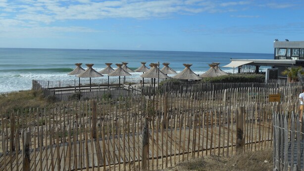 Une vue sur la plage avec une clôture en bois, des parasols de plage et un bâtiment en arrière-plan.