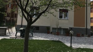 En byggnad med ett platt tak, en stenlagd innergård och ett träd i förgrunden.