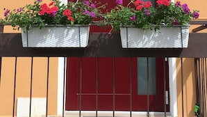 En byggnad med en röd dörr, två blomlådor på balkongen och en skylt ovanför dörren.
