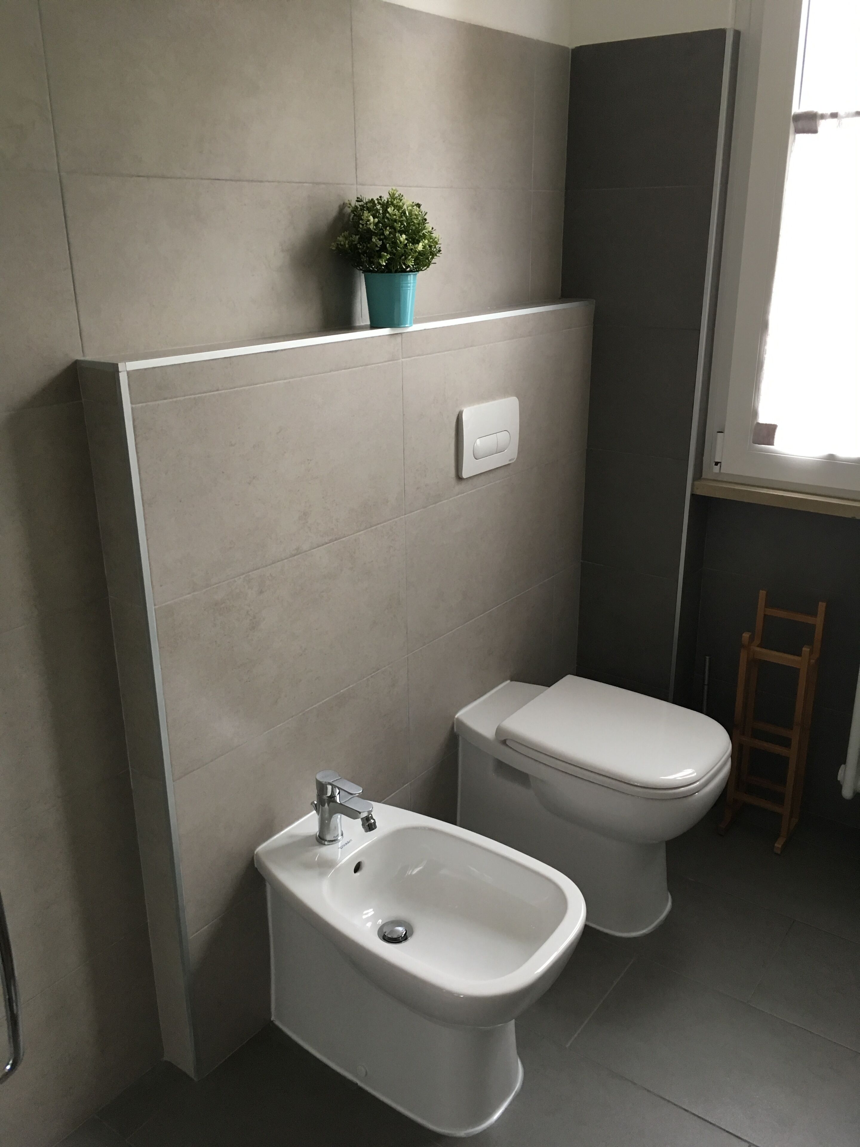 Un baño moderno con bidé, inodoro y una pequeña planta en maceta en la pared.