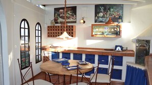 A dining area with a round wooden table, four chairs, a hanging light fixture, and blue storage bins under the counter. - La casa del molino-Ideal for Two (Mogan)