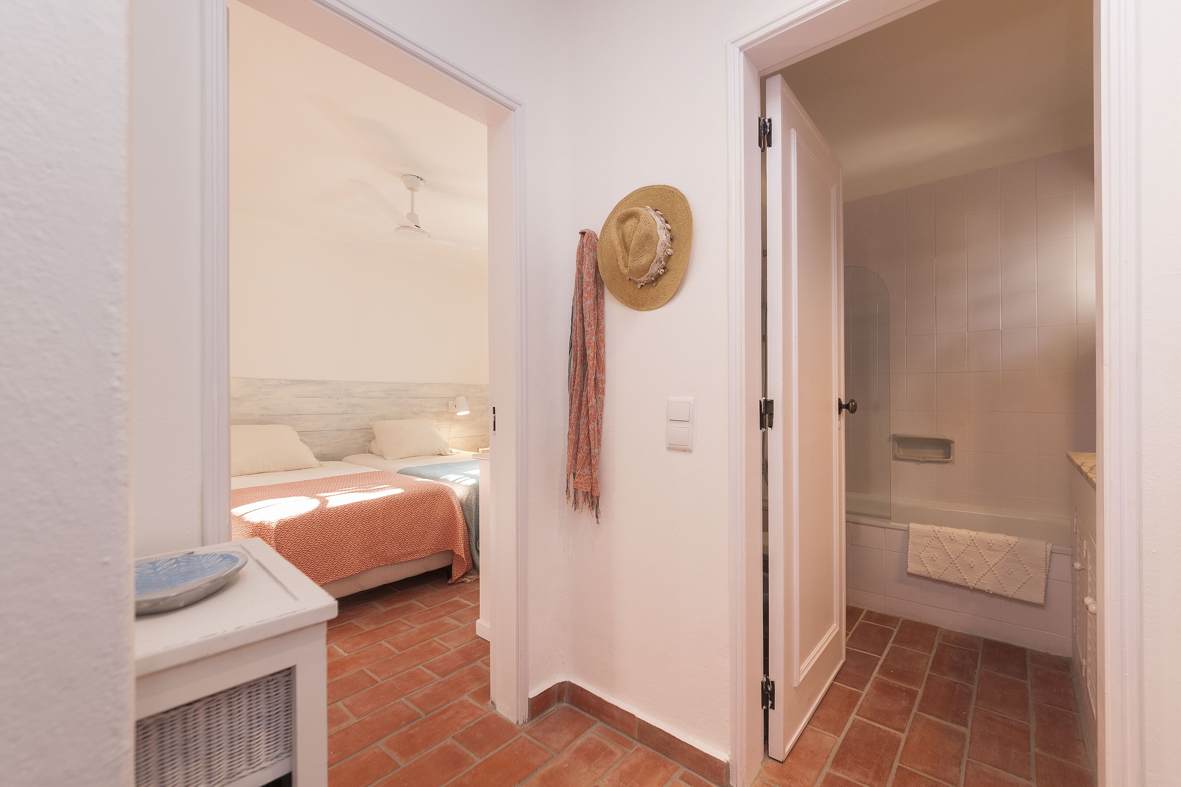 A bathroom with a shower, a towel rack, and a bed visible through an open door.
