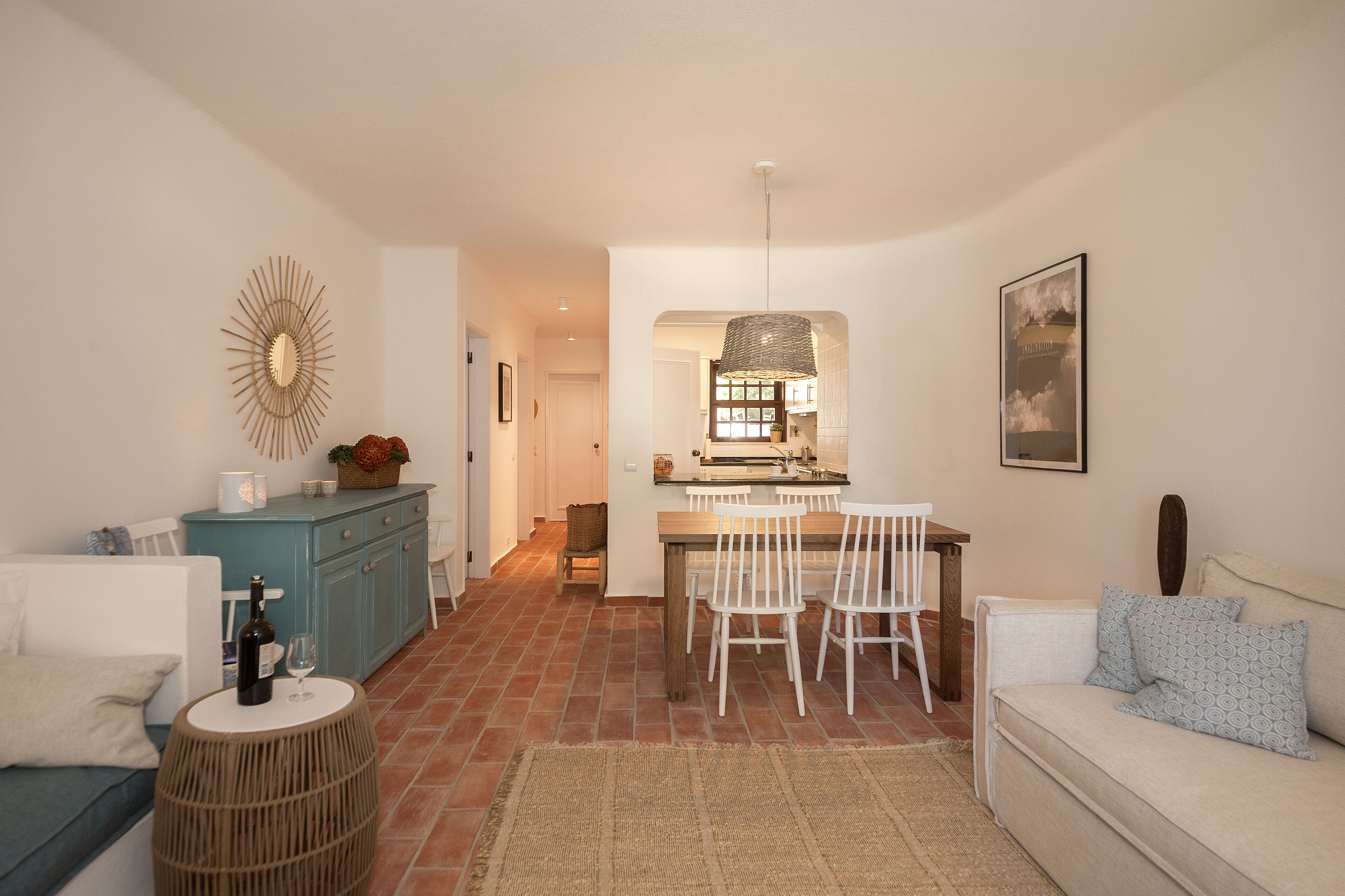 A modern kitchen with a dining area, white furniture, and a rustic floor.